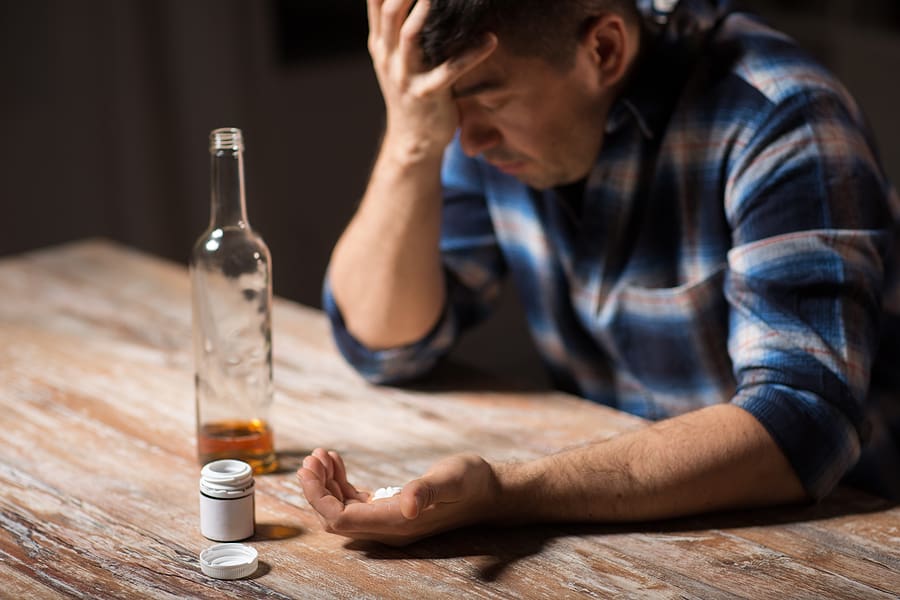 Sad man holding a handful of bills with a bottle of alcohol in front of him