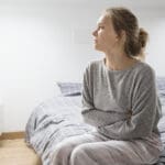 Young depressed veteran with stomach issues sitting on her bed looking sad