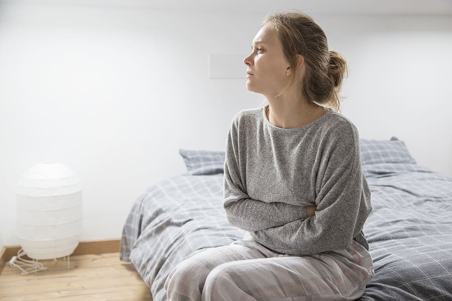 Young depressed veteran with stomach issues sitting on her bed looking sad