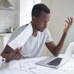 Veteran looking frustrated while holding paperwork for a VA claim appeal and looking at his laptop