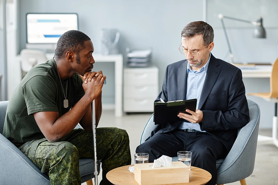 Veteran with cane sits on couch speaking to a VA provider about his disability
