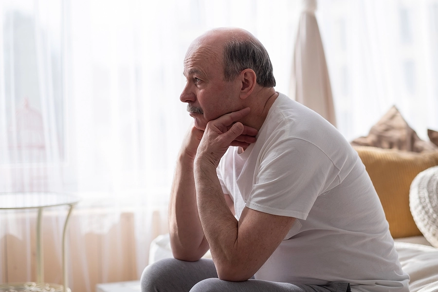 Male veteran dealing with erectile dysfunction (ED) sitting on a bed at home