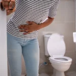 Female veteran with a gastrointestinal disorder clutches her stomach in pain after using the bathroom